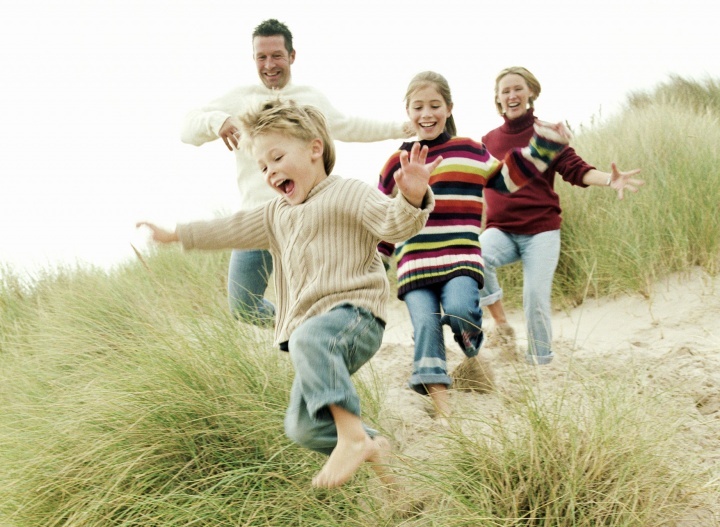 Uma família correndo na praia com grama.