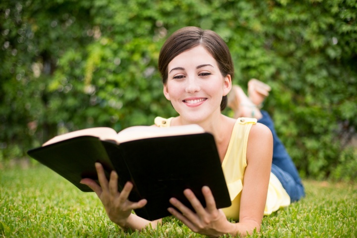 Uma mulher lendo uma Bíblia num campo de relva.