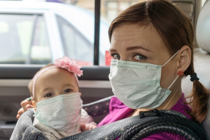 Uma mulher e uma criança pequena usando máscaras, sentados num carro.