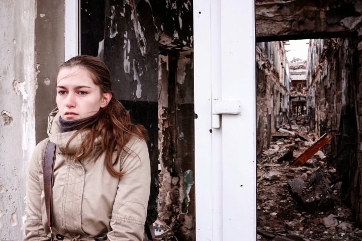 A young woman standing outside a crumbling building.