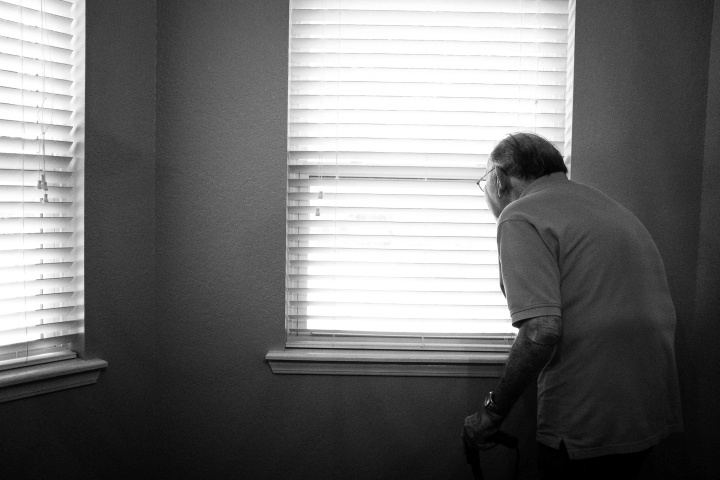 Um homem idoso olhando pela janela.