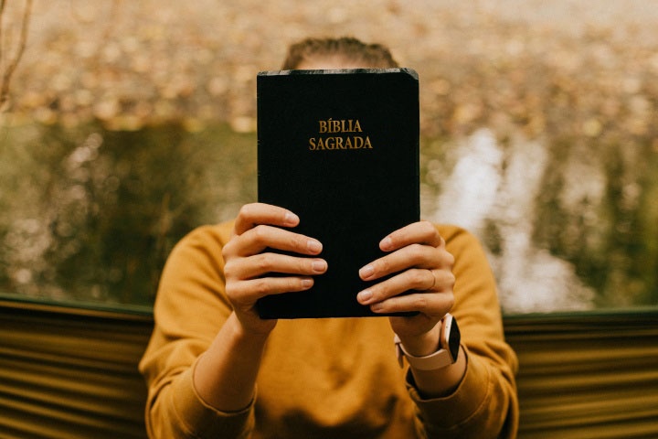 Uma mulher segurando uma Bíblia na frente do rosto. 