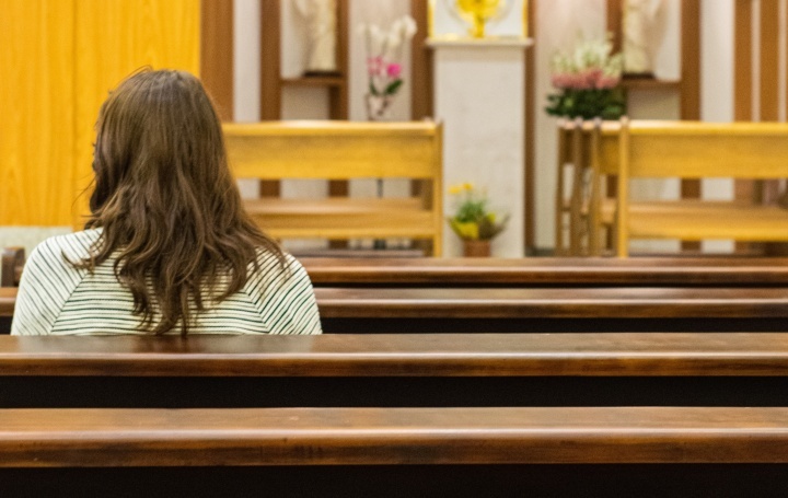 Uma mulher sentada num banco de uma igreja.