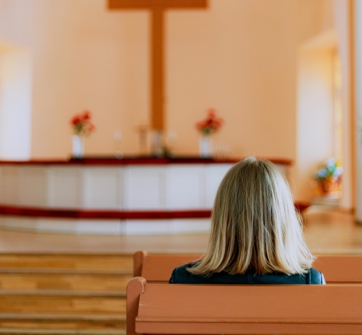 Deus é muito específico na Bíblia sobre como Ele deseja ser honrado — e não é da maneira que acharmos melhor, mas da maneira como Ele instrui. Uma mulher num banco de uma igreja olhando para o altar e a cruz.
