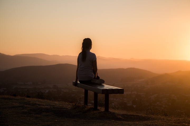 Uma mulher sentada em um banco observando o pôr do sol.