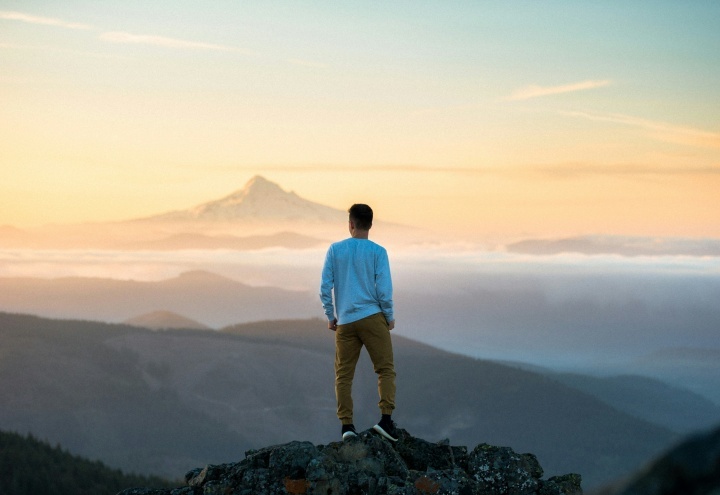 Um jovem em pé sobre uma rocha olhando para uma paisagem.