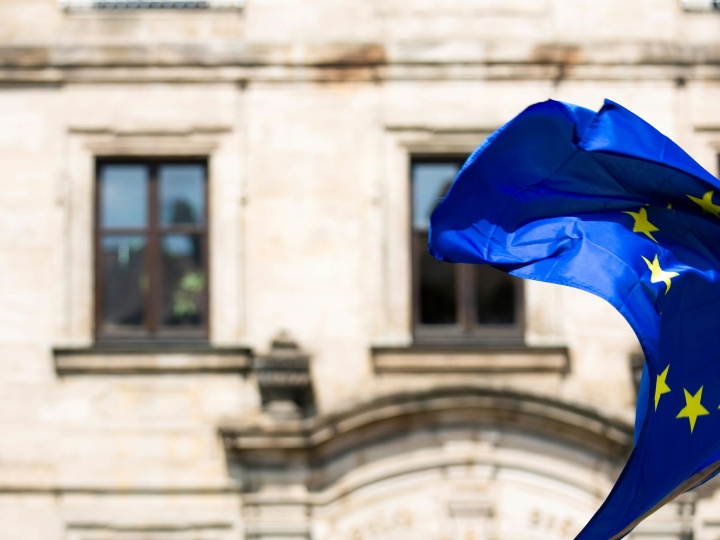 A União Europeia enfrenta fortes ventos de mudança — e seu futuro está sendo moldado rapidamente enquanto a história, a política e a profecia convergem. Uma bandeira da União Europeia tremulando ao vento defronte a um prédio antigo.