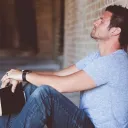 Um homem segurando sua Bíblia de costas a uma parede - com os olhos fechados e orando.