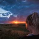Uma mulher num campo com o pôr do sol à distância.