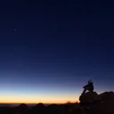 Uma pessoa sentada numa pedra ao pôr do sol.