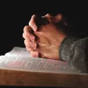 Mãos entrelaçadas em cima de uma Bíblia aberta.