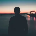 Uma pessoa admirando um pôr-do-sol sobre água.