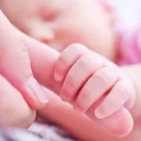 Um bebê segurando os dedos da mãe.