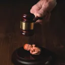 Uma ilustração dum bebê recém-nascido debaixo do martelo dum juiz.