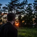 Um homem com o sol atrás das árvores.