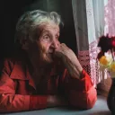 Uma senhora idosa sentada perto duma janela, olhando para fora.