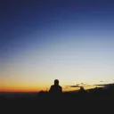 Uma pessoa sentada no topo da colina olhando para a extensão do céu noturno.