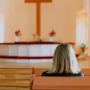 Uma mulher num banco de uma igreja olhando para o altar e a cruz.