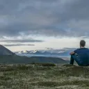 Um jovem sentado na grama olhando para as montanhas.