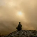 Uma pessoa sentada em uma pedra no meio da neblina matinal.