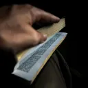 Mão folheando páginas de uma Bíblia.