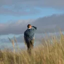 Um homem caminhando em um campo e olhando para as nuvens.