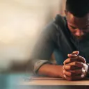 Um homem orando sentado à mesa.