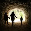 Família de três pessoas caminhando em uma caverna em direção à luz.