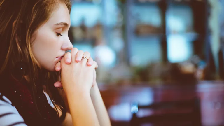 Deus nem sempre responde as nossas orações para nos livrar imediata e instantaneamente de nossas aflições. Mas Ele sempre fará o que for melhor para nós. Uma jovem orando.