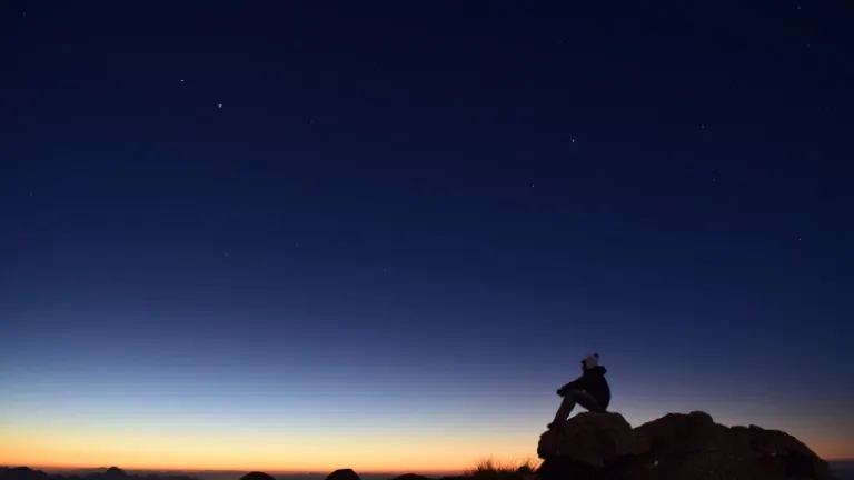 Uma pessoa sentada numa pedra ao pôr do sol.