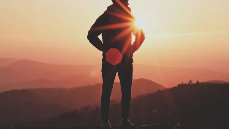 Uma pessoa de pé numa rocha com o sol atrás deles.
