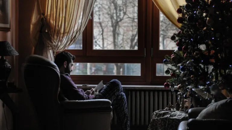 Um homem sentado em uma cadeira em frente a uma árvore de Natal.