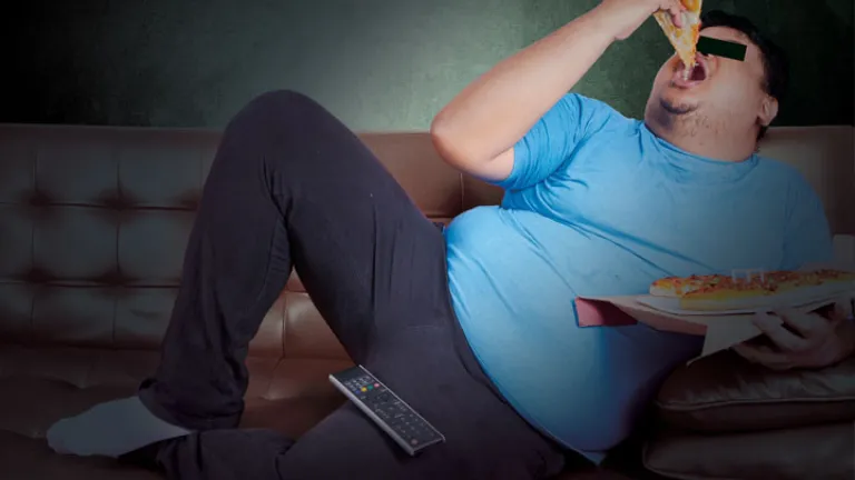 Um sujeito preguiçoso que come uma fatia de pizza em um treinador ao prestar atenção à tevê.