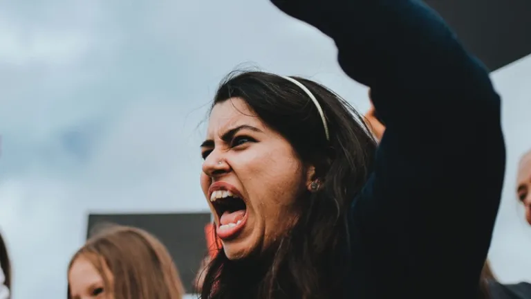 Uma mulher furiosa gritando com o punho no ar.