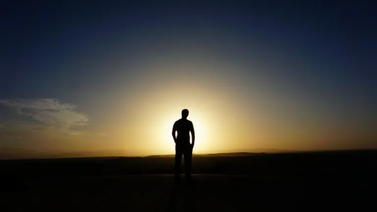 Um homem andando em um campo com os raios de sol brilhando sobre ele.