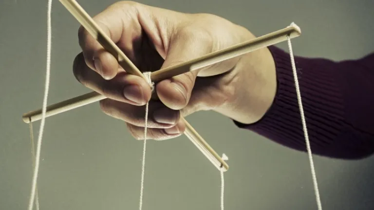 Uma pessoa segurando cordas de uma marionete.