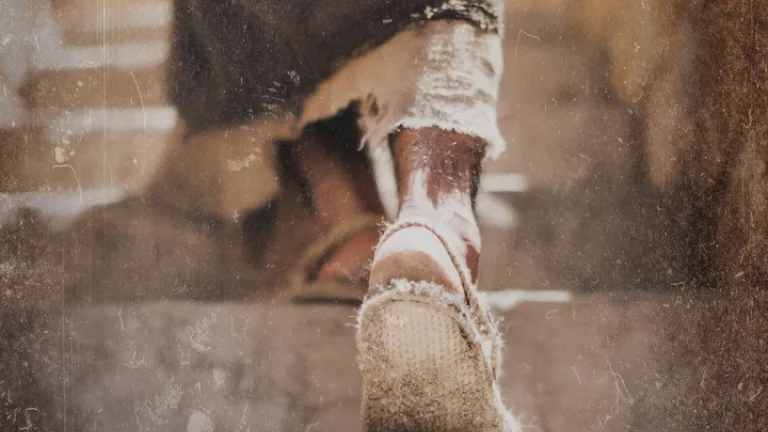 Uma pessoa de sandálias subindo uma escadaria empoeirada.