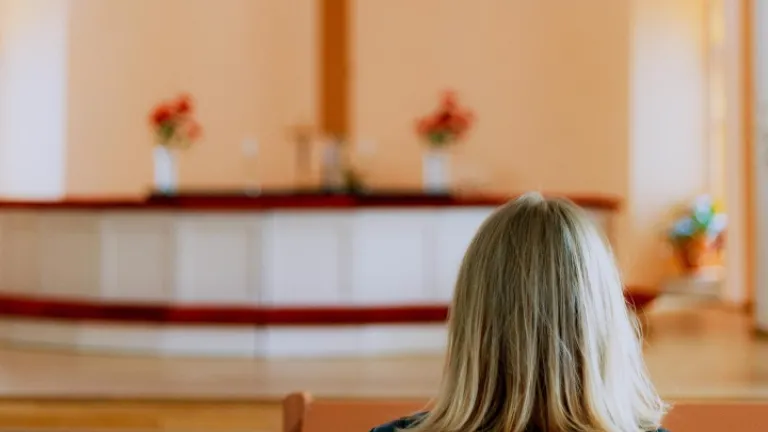 Uma mulher num banco de uma igreja olhando para o altar e a cruz.