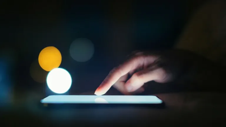 Um dedo tocando na tela iluminada de um dispositivo eletrônico.