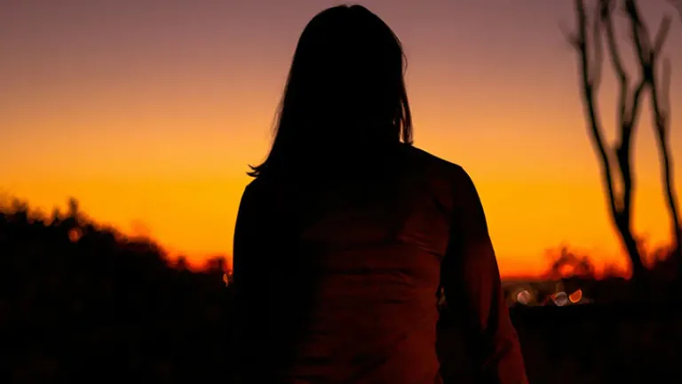 Silhueta de mulher refletindo sobre a vida com o pôr do sol ao fundo.