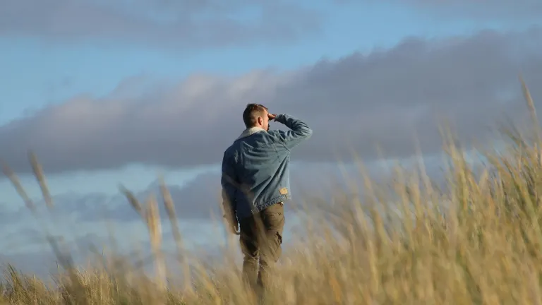 Um homem caminhando em um campo e olhando para as nuvens.