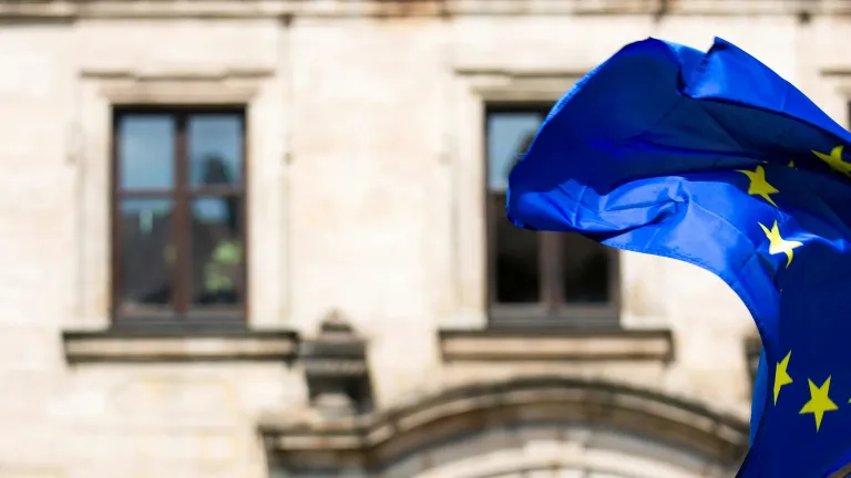 Uma bandeira da União Europeia tremulando ao vento defronte a um prédio antigo.