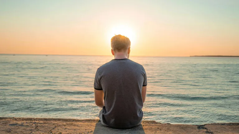 Um homem cabisbaixo sentado na orla da praia.