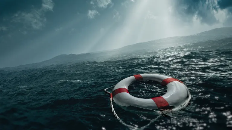 Uma boia salva-vidas à deriva em um mar agitado sob a luz solar que atravessa as nuvens.