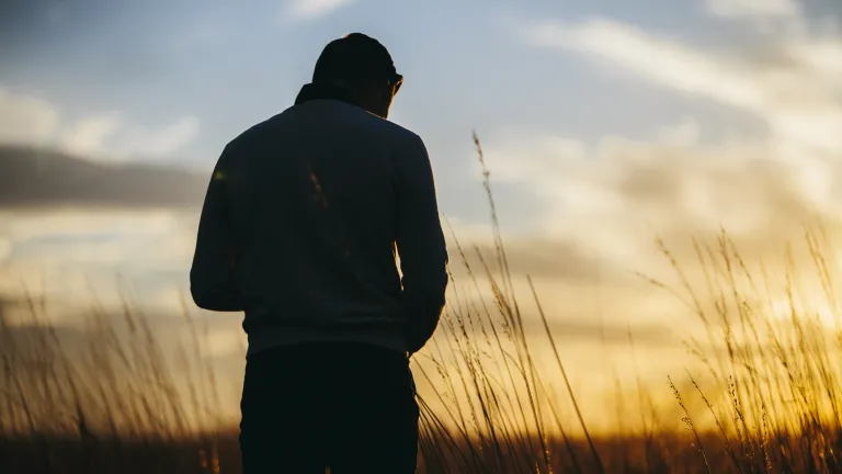 A silhueta de um jovem com o pôr do sol ao fundo.