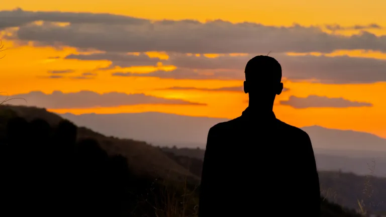 As instituições humanas podem fracassar, mas a fé e obediência a Deus hoje nos preparam para o iminente Reino de Cristo. Uma pessoa observando um vale ao entardecer.