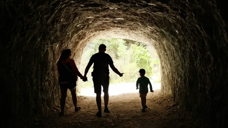 Família de três pessoas caminhando em uma caverna em direção à luz.
