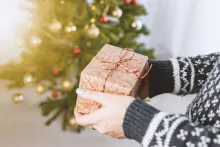 Uma pessoa segurando um presente embrulhado na frente de uma árvore de Natal.