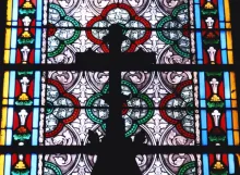 Uma cruz e um vitral dentro de uma grande igreja.