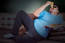 Um sujeito preguiçoso que come uma fatia de pizza em um treinador ao prestar atenção à tevê.